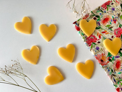 Heart-shaped beeswax refresher bars for beeswax wraps and bags on a white surface with a floral breadbag.