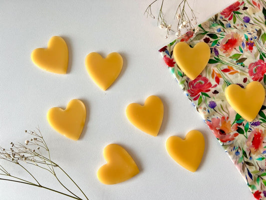 Heart-shaped beeswax refresher bars for beeswax wraps and bags on a white surface with a floral breadbag.