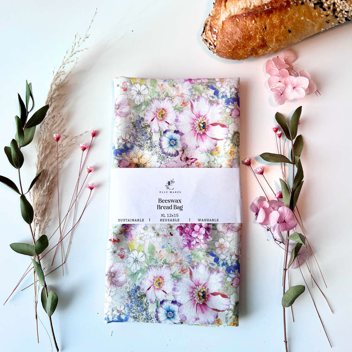 Pink floral-patterned beeswax bread bag on a white surface with bread and flowers.