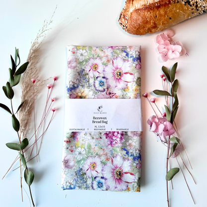 Pink floral-patterned beeswax bread bag on a white surface with bread and flowers.